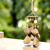 Handmade natural seed pod wind chime with large polished brown fruit shells hanging from a carved wooden canopy disk in soft green garden light