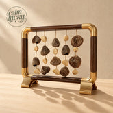 Handmade desktop seed chime with five hanging strands of dark textured pods and smooth ivory seeds in a walnut wood and brass tabletop frame, calming natural office and home decor on beige background