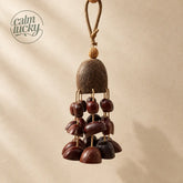 Handmade forest seed shell wind chime with polished reddish-brown half-shells and natural beige seeds under a coconut dome, warm beige studio background