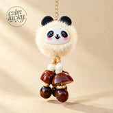 Cute fluffy cream panda plush keychain with black ears and rosy cheeks, dangling polished dark brown seed pod rattle bells and wooden beads on a gold keyring, handmade lucky bag charm on beige background