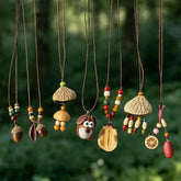 Handmade natural seed necklaces with acorn, nut shell and carved wood pendants on adjustable cords, hanging against a green forest background