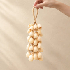 Hand holding a handmade handheld tano phoenix egg seed wind chime with smooth cream-colored seeds