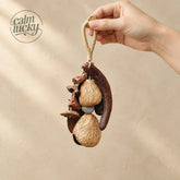 Hand holding a handmade natural wild seed pod bag charm and keychain with carved wooden flower beads, two beige bell pods and dark seeds on a twine loop, boho nature accessory on beige background