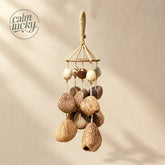 Handmade hanging seed pod wind chime with large textured natural brown nuts clustered below small ivory, striped and patterned beads on a wooden ring and woven cord loop, calming forest canopy decor on beige background