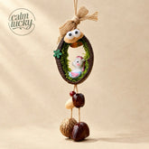 Handmade Chinese zodiac horse lucky seed chime, a cute white pony figurine with pink mane nestled in a moss-lined walnut shell ring with googly eyes and a twine bow, polished seed pods hanging below, whimsical gift charm on beige background