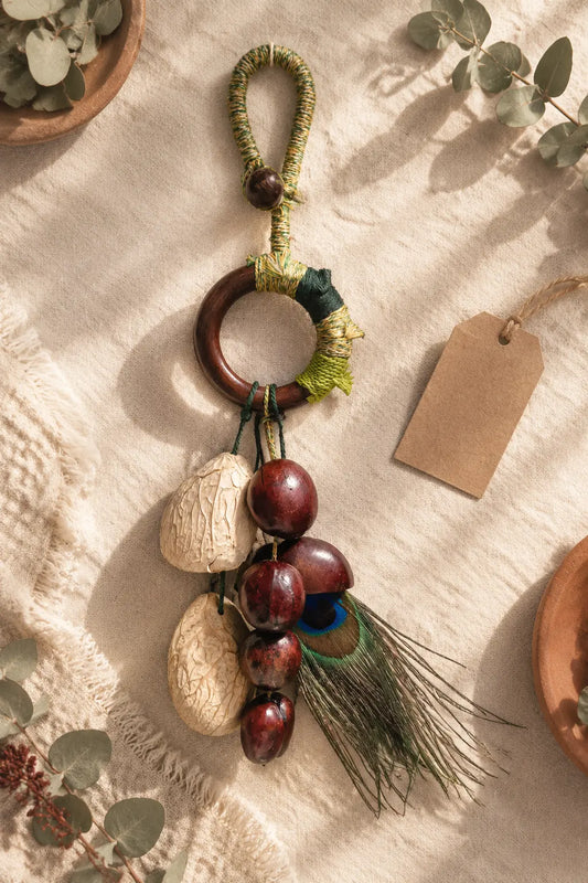 Handmade natural seed lucky charms — shell bag charm, seed necklace, phone charm and zodiac figure — arranged on cream linen.