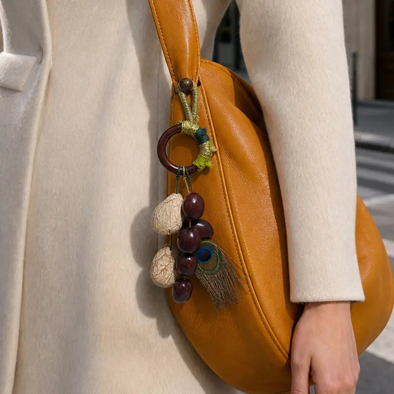 Side view of mustard leather bag featuring natural seed charm with wooden ring and peacock feather