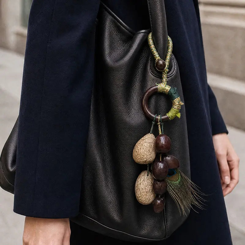 Handcrafted natural seed bag charm with peacock feather on black leather handbag, artisan boho accessory
