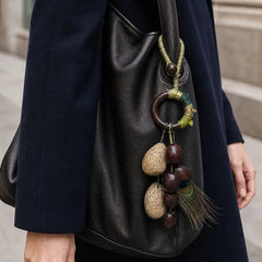 Handcrafted natural seed bag charm with peacock feather on black leather handbag, artisan boho accessory