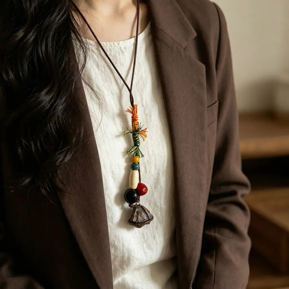 Festival Wrap natural seed necklace — colorful thread-wrapped cord with black and red bead cluster, handmade boho pendant on adjustable cord