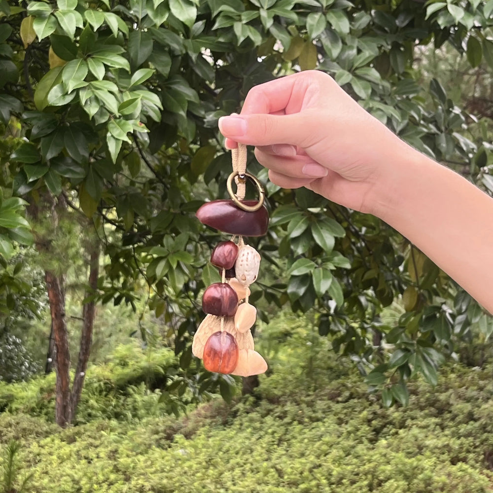 Handmade Amber Harvest bag charm with deep red-brown glossy seeds and cream shells on brass ring, warm earthy boho accessory