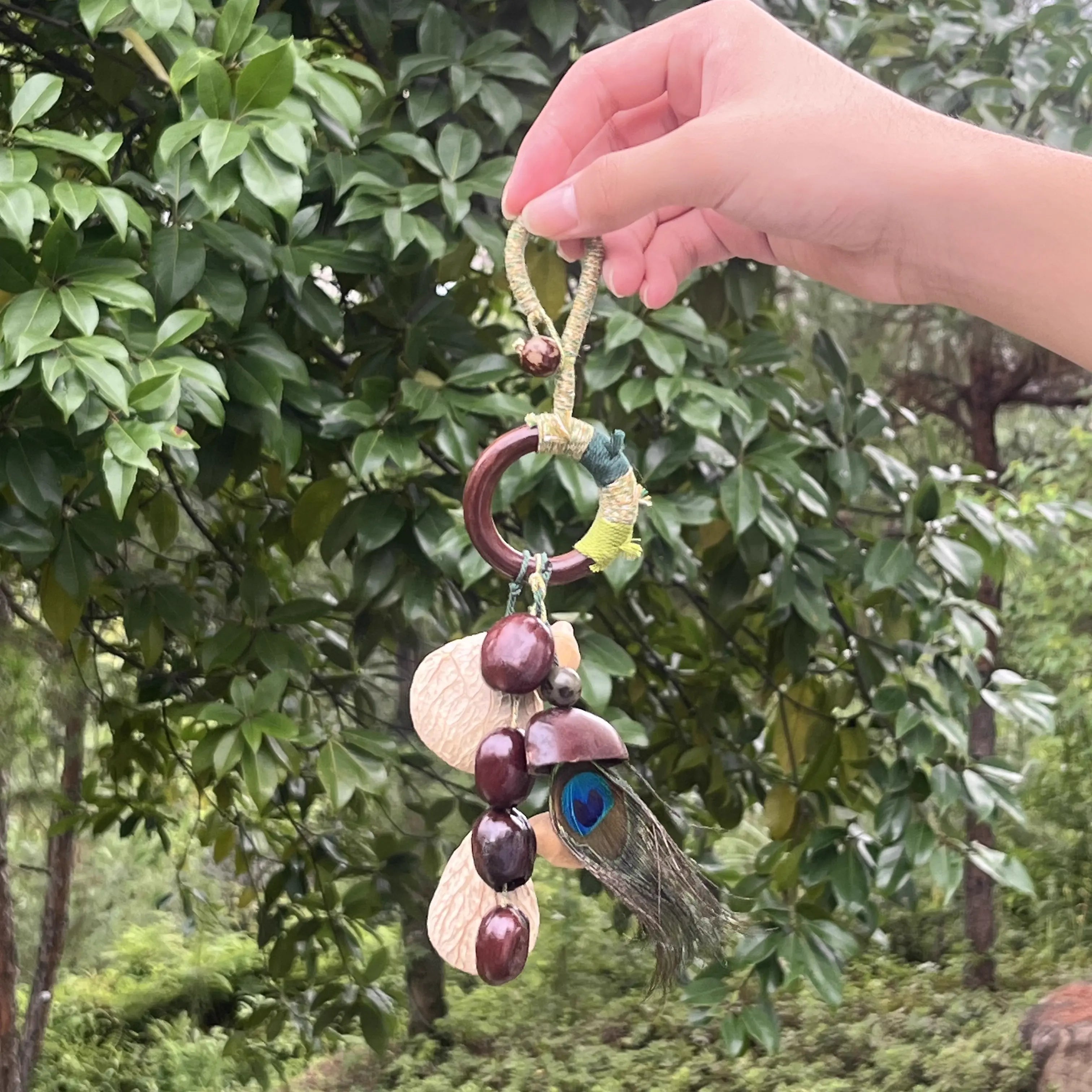 Handmade Peacock Feather bag charm with real iridescent peacock feather, natural seeds and shells on green and gold thread-wrapped ring