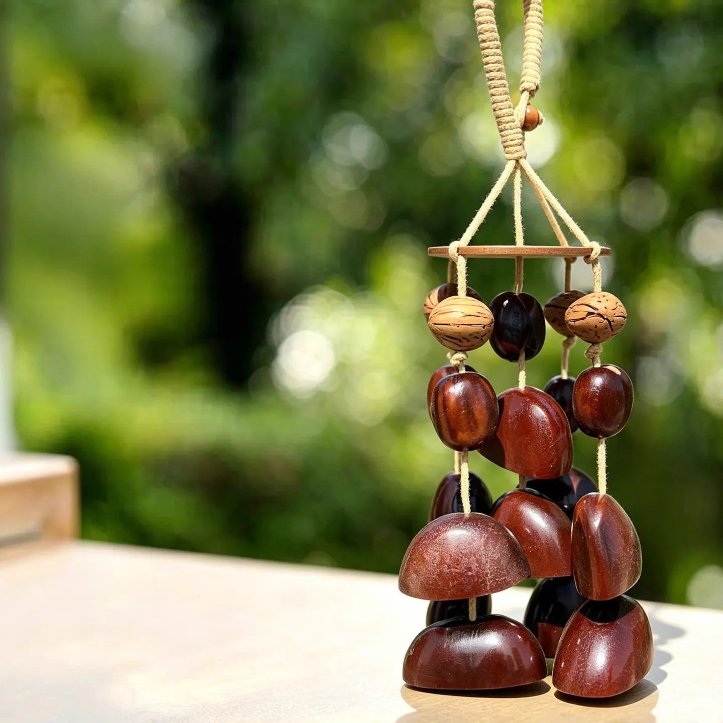 Handmade wind chime of polished mahogany-brown seed pods and patterned nuts tiered from a wooden canopy disk outdoors