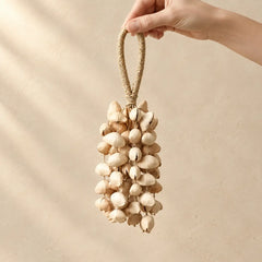 Hand holding a handmade handheld chacha oleander seed wind chime strung with small cream-colored seeds