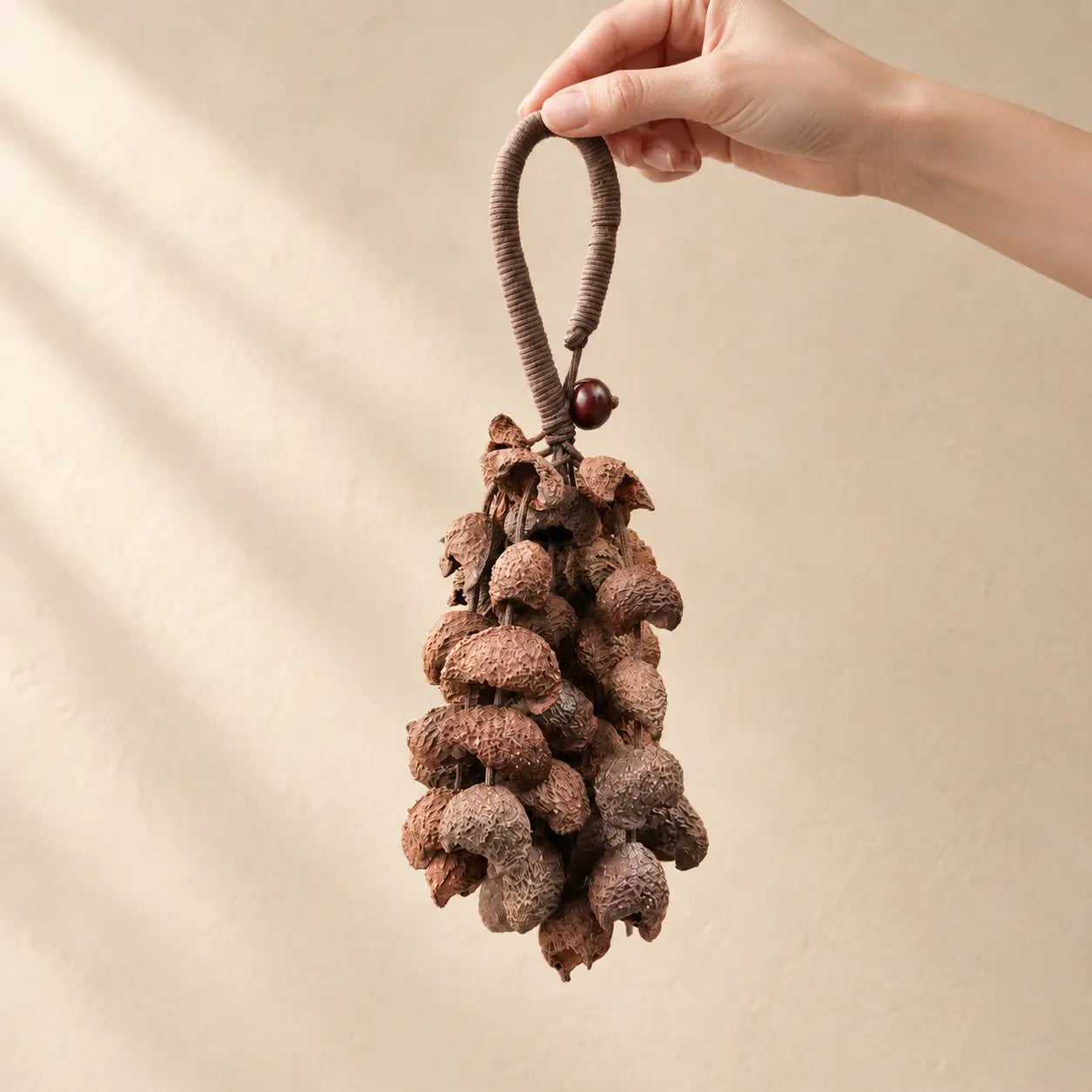 Hand holding a handmade handheld moonin wind chime strung with brown crescent-shaped seed pods