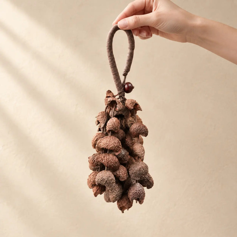 Hand holding a handmade handheld moonin wind chime strung with brown crescent-shaped seed pods