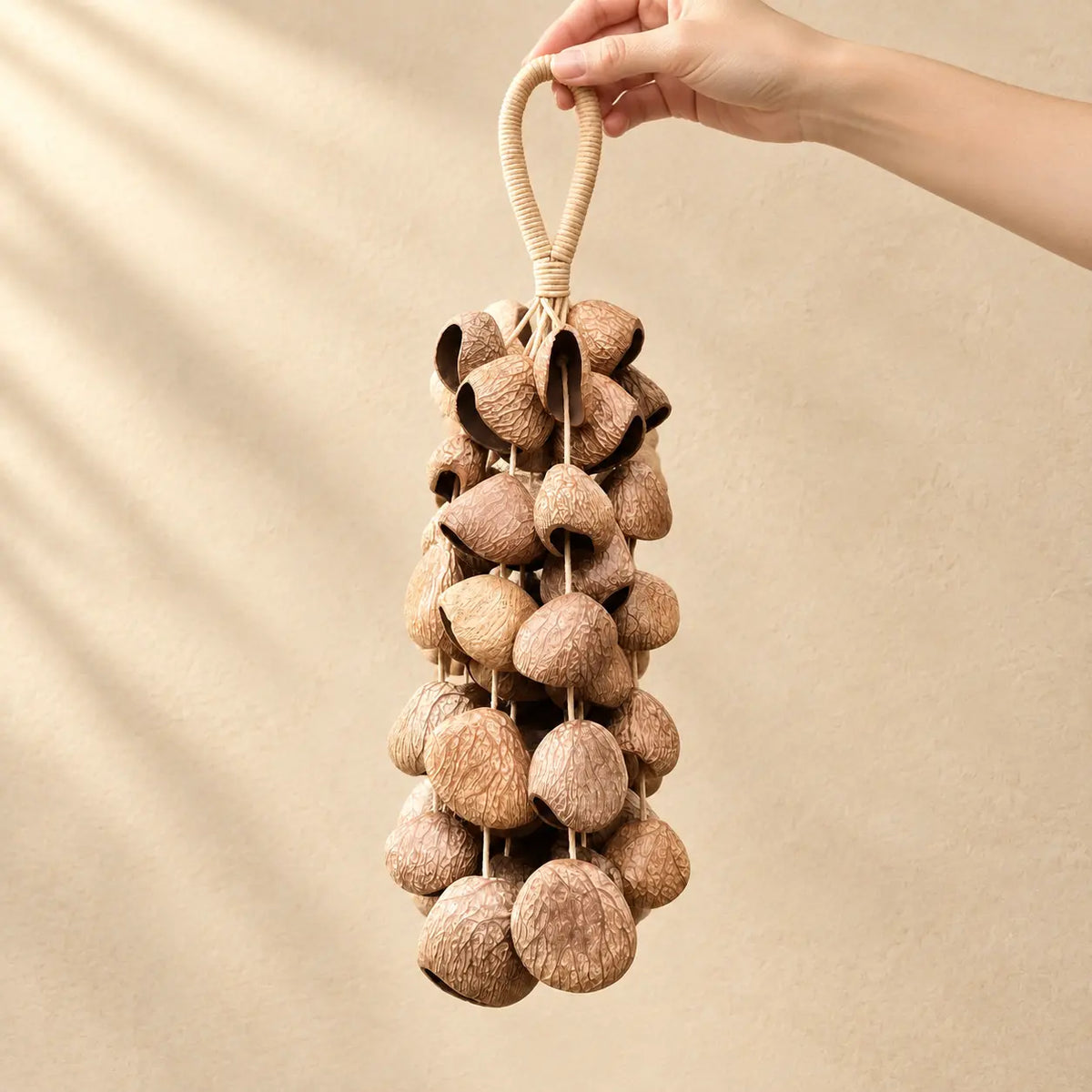 Hand holding a handmade handheld panji pangium edule seed wind chime with dark brown nuts