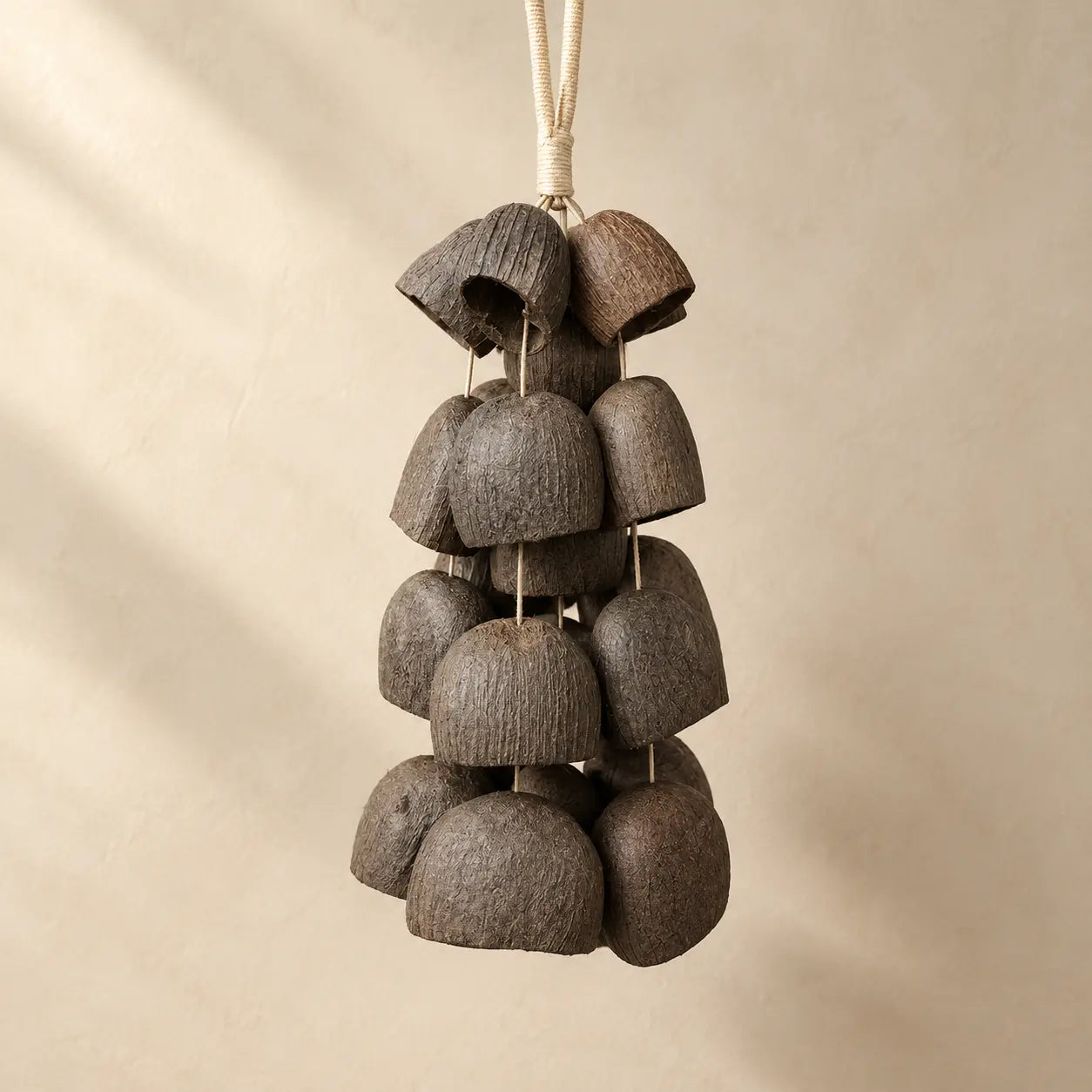 Salin coconut shell wind chime with 24 half coconut shells on natural fiber rope, earthy brown, hanging against beige wall