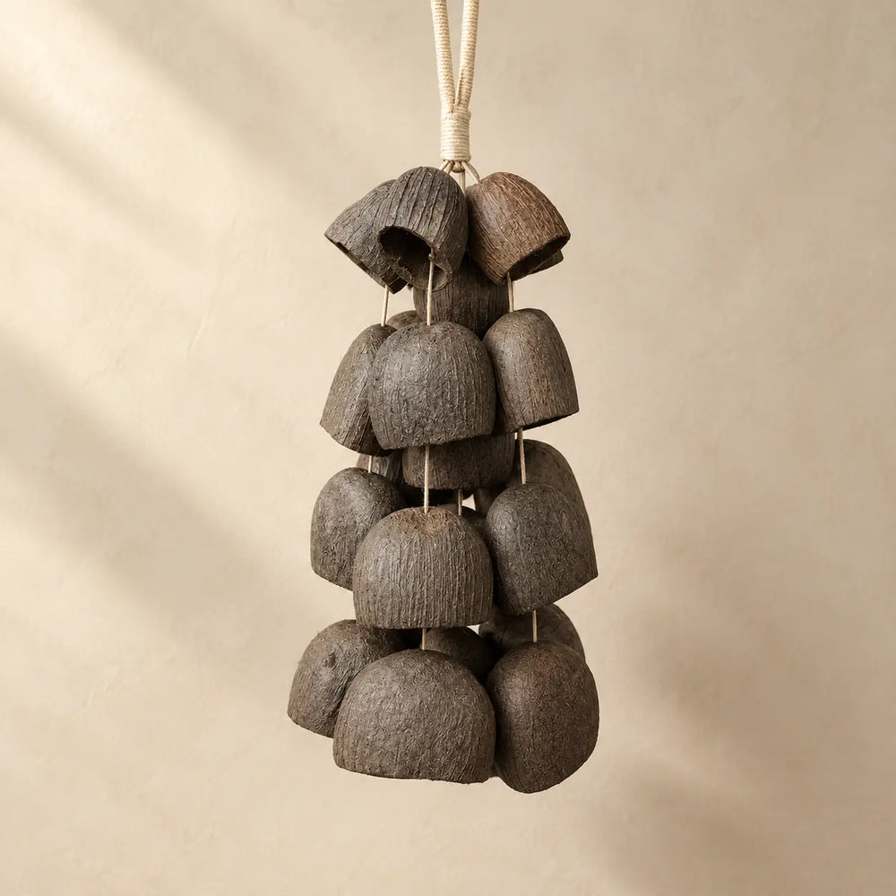 Salin coconut shell wind chime with 24 half coconut shells on natural fiber rope, earthy brown, hanging against beige wall