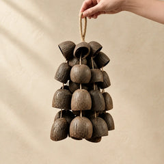 Hand holding a handmade handheld salin water bellwood seed wind chime strung with layered dark brown bell-shaped seeds