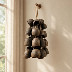 Handmade salin water bellwood seed chime with dark bell-shaped pods hanging by a bright window with sheer curtains