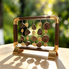 Wish of Ages — light walnut with gold corner accents, five strings of dark chocolate half-shells and whole oval seeds, backlit on a wood desk