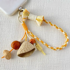 Honey Bell seed phone charm — golden yellow braided wrist strap with nut shell bell, brown wood bead and orange ceramic star bead