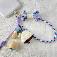Indigo Willow seed phone charm — purple and teal hand-braided wrist strap with pale nut shell bells and blue glazed ceramic bead