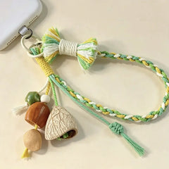Jade Sprig seed phone charm — green and yellow hand-braided wrist strap with shell bells and wooden beads, clipped to a phone