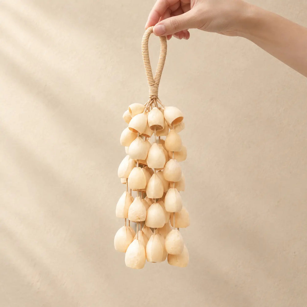Hand holding a handmade handheld tano phoenix egg seed wind chime with smooth cream-colored seeds