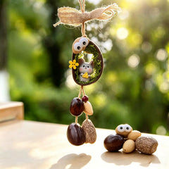 Rat zodiac chime — cute gray mouse holding cheese, nestled in a mossy nut shell with googly eyes and seed bells, garden bokeh background